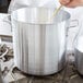 A person stirring a Vollrath Arkadia aluminum stock pot with a wooden spoon.