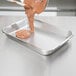 A person's hand pouring brown substance into a Vollrath stainless steel roasting pan.