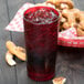 A red Cambro plastic tumbler filled with ice and a red drink on a table with a basket of pretzels.