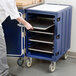 A person putting trays in a blue Cambro cart.