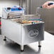 A hand holding a basket of food over a Globe electric countertop fryer.