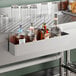 A stainless steel single tier speed rail mounted to a bar counter, holding several liquor bottles.