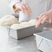 A person's hands reaching for dough in a Chicago Metallic bread loaf pan.