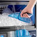 A person using a blue San Jamar Saf-T-Scoop to get ice from a machine.