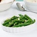 A white fluted oval serving dish filled with green beans with a spoon next to it.