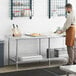 A man in an apron standing at a Regency stainless steel work table.