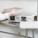 A person in a white coat loading a Cambro food pan carrier.