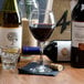 A Libbey red wine glass filled with red wine on a table with wine bottles.