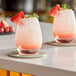 Two Libbey spirits glasses with pink drinks and fruit on top.