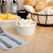 A Tuxton eggshell ramekin filled with food on a table with silverware and a salt shaker.
