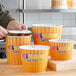 A person putting food into a Choice hot food bucket with a lid.