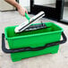 A hand holding a green Unger bucket with a black handle and a green brush.