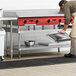 A man in an apron using a Regency stainless steel equipment stand to hold a metal pan.