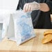 A person in white gloves using a Printed Plastic Deli Saddle Bag to hold a bag of donuts.