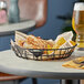 A black American Metalcraft wire basket on a table with a bowl of food in it.