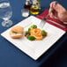 A hand holding an Arcoroc porcelain plate with food, a fork, and a knife.