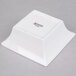 An Arcoroc white square flared bowl with a black logo.