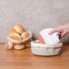 A hand holding a white towel in a basket next to a white bread warming stone.