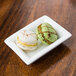 A white rectangular bowl filled with two macarons on a wood surface.