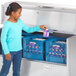 A girl standing next to a Traulsen milk cooler in a school kitchen opening the door.