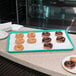 A Carlisle teal Glasteel bakery display tray of chocolate covered doughnuts on a counter.