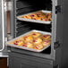 A Carlisle Cateraide front loading black insulated food pan carrier holding trays of pastries in an oven.