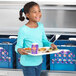 A young girl holding a tray of food in front of a Traulsen school milk cooler.
