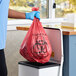 A hand in blue gloves holding a red plastic bag.