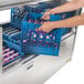 A person using a blue Traulsen milk crate to fill a blue Traulsen milk cooler on a counter in a school kitchen.