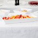 A rectangular white melamine bowl filled with fruit on a white table.