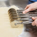 A hand holding a metal Ateco pastry cutter with six small wheels.