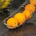 A Tablecraft curved metal fruit basket holding oranges.
