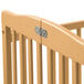 A natural wood L.A. Baby mini crib with metal bars.