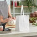 A woman in an apron using white Choice paper bag with handles to wrap a jar.