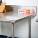 A stainless steel Advance Tabco work table with a box on the undershelf.