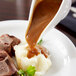 A white porcelain gravy boat pouring gravy over a plate of meat and mashed potatoes.