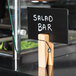 An American Metalcraft natural clothespin table card holder with a small black sign clipped in it.