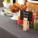 A table with a white bowl of carrot juice and a sign held by an American Metalcraft natural clothespin card holder.