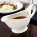 An American Metalcraft white porcelain gravy boat with brown gravy on a table.