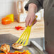 A hand holding a yellow Mercer Culinary slotted spatula over a pan of food.