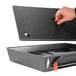 A hand opening a black rectangular container with a black rectangular pan inside.