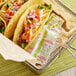 A table with a metal tray of tacos and a bowl of condiment packets.