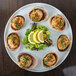 A Cal-Mil round porcelain platter with clams, salad, and a lemon slice on a table.