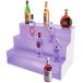 A Cal-Mil 3 step bottle display with bottles of alcohol on each shelf, with LED lights.