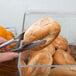 A person using tongs to grab a bagel from a Cal-Mil Classic Acrylic food bin filled with bagels.