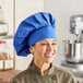 A royal blue 13-inch chef hat worn by a person in a kitchen setting.