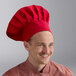 A man wearing a large red chef hat and a matching red chef coat.