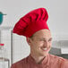 A red chef hat being worn by a person in a kitchen setting.