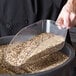 A person using a Cal-Mil polycarbonate scoop to pour grains into a container.