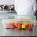 A chef standing in a school kitchen with a Carlisle green food storage box filled with red bell peppers.